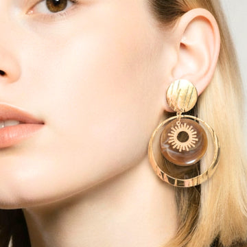 Femme portant des boucles d’oreilles pendantes dorées avec médaillon marron et motif soleil