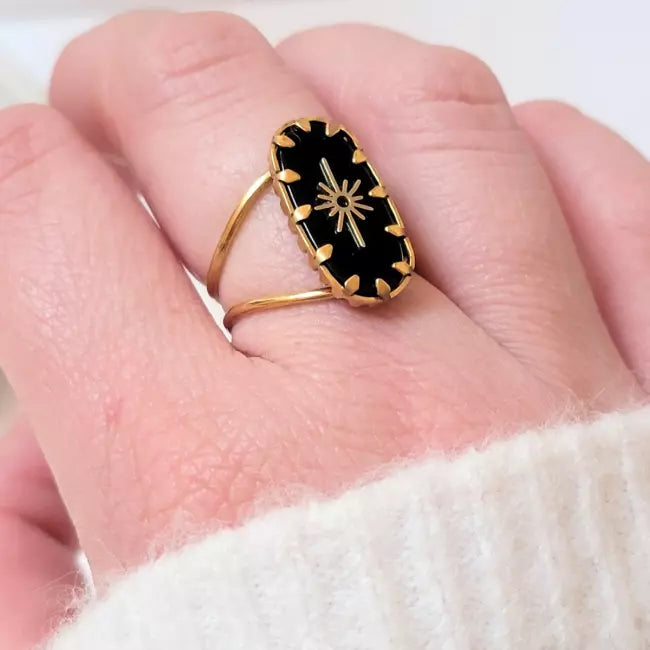 Bague dorée avec pierre noire portée au doigt femme