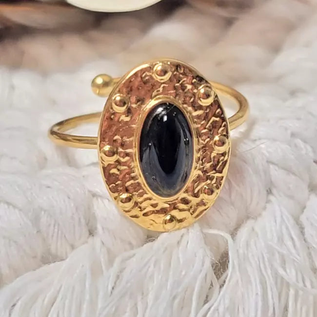 Bague ajustable dorée en acier inoxydable avec pierre noire ovale sur fond blanc