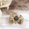 Bague dorée multi-rangs avec cabochon central labradorite, acier inoxydable ajustable — présentation sur fond blanc et fleurs séchées.