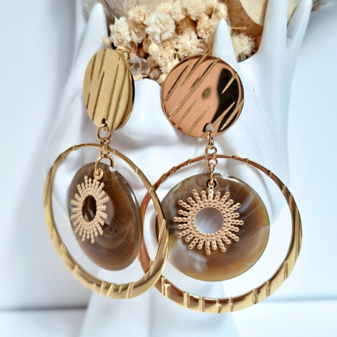 Femme portant des boucles d’oreilles pendantes dorées avec médaillon marron et motif soleil