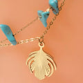 Gros plan pendentif feuille dorée sur bracelet de cheville turquoise