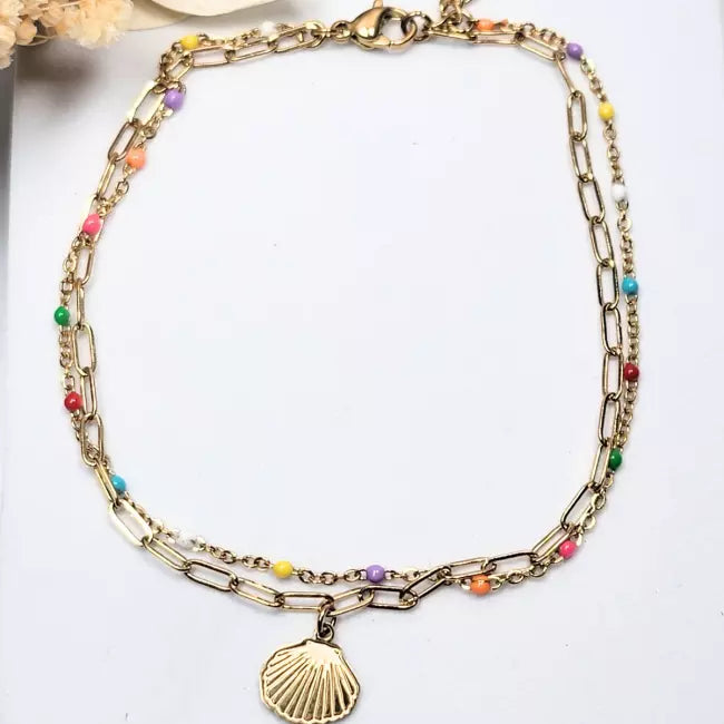 Détail chaîne de cheville dorée avec pendentif coquillage et petites perles multicolores