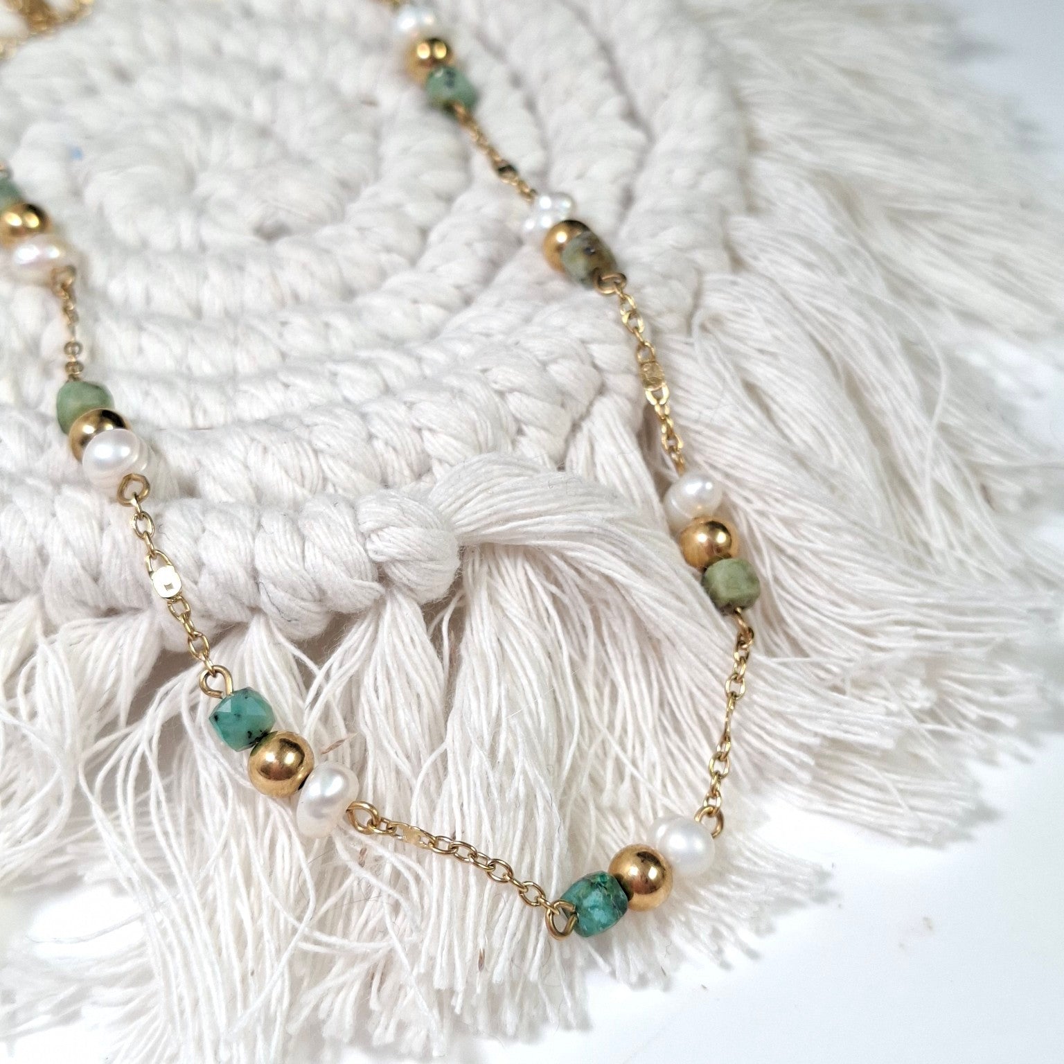 Collier ras-de-cou doré avec perles irrégulières blanches et perles facettées vert d’eau, posé sur support macramé.
