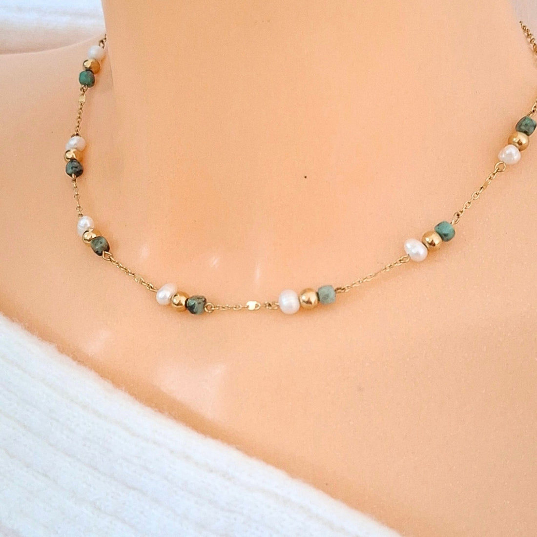 Collier ras-de-cou fin doré avec perles blanches irrégulières et perles facettées vert d’eau porté autour du cou.