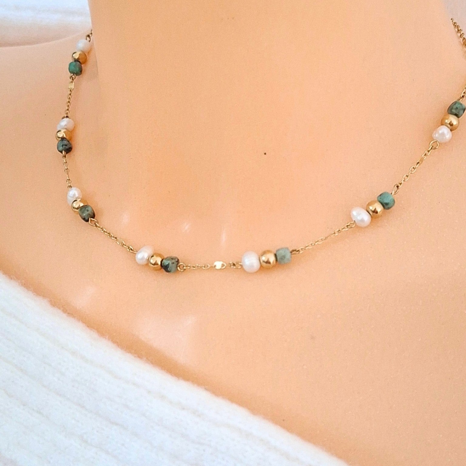 Collier ras-de-cou fin doré avec perles blanches irrégulières et perles facettées vert d’eau porté autour du cou.