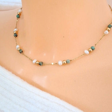 Collier ras-de-cou fin doré avec perles blanches irrégulières et perles facettées vert d’eau porté autour du cou.