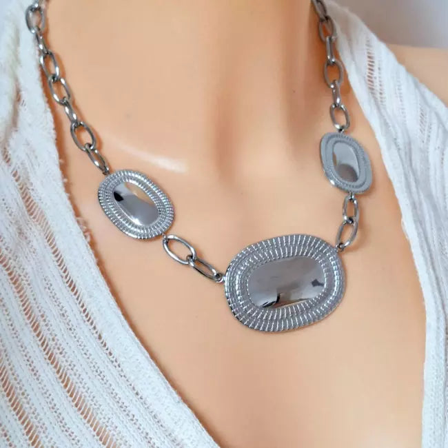 Collier large argenté en acier inoxydable porté, avec pendentifs ovales texturés style vintage chic.