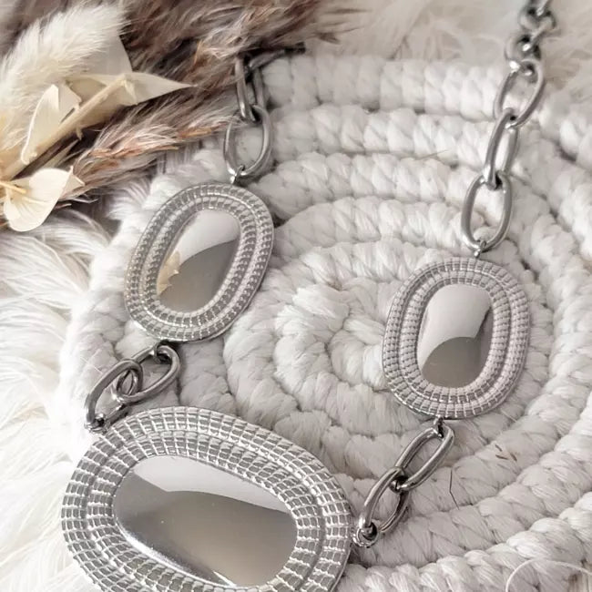 Collier large argenté en acier inoxydable, pendentifs ovales texturés reliés par maillons, gros plan.