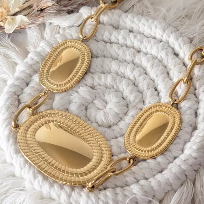 Collier large doré en acier inoxydable, trois pendentifs ovales texturés reliés par maillons, vu de dessus.