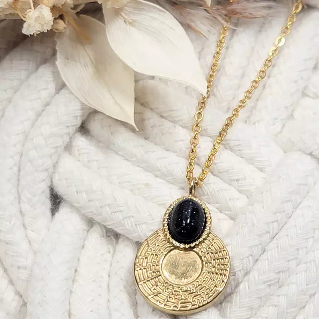 Collier pendentif doré porté – chaîne fine et médaillon rond texturé avec cabochon bleu pailleté, aperçu de la longueur sur le décolleté.
