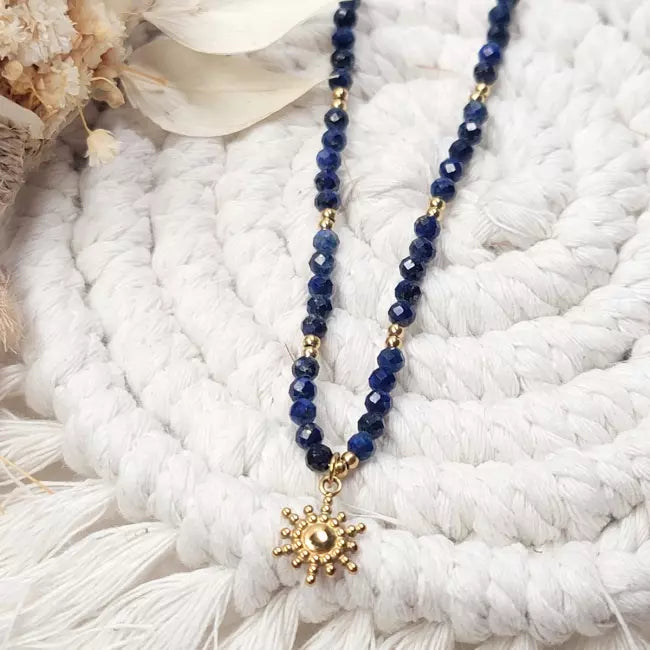 Collier soleil doré avec perles facettées bleu marine, pendentif doré en forme de soleil.