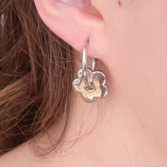 Boucles d’oreilles créoles fleurs argentées en acier inoxydable portées par une femme