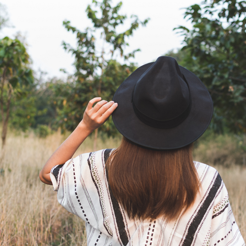femme de dos dans un champ, elle porte des habits bohèmes et un chapeau