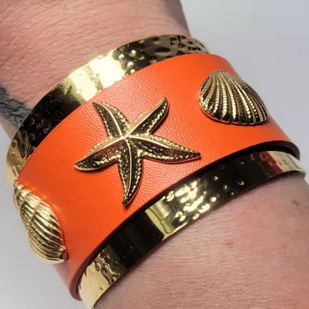 Bracelet manchette orange porté, finition dorée martelée et motifs coquillages brillants