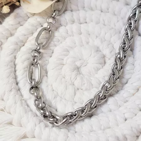 Gros plan sur le collier en acier inoxydable argenté avec maillons ovales et chaîne tressée, posé sur fond blanc en corde tressée