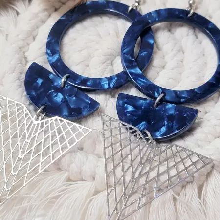 Paire de boucles d’oreilles géométriques bleu nuit et argentées posée sur fond macramé bohème