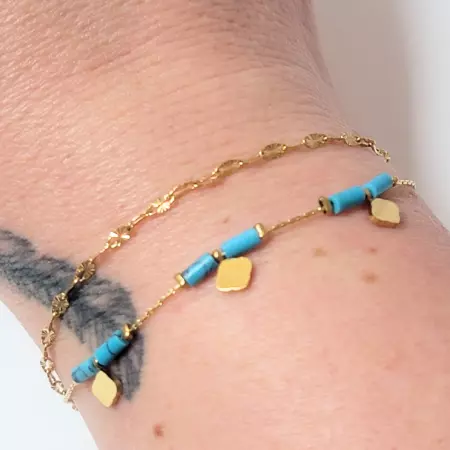 Bracelet doré porté au poignet, perles turquoises et pampilles dorées visibles