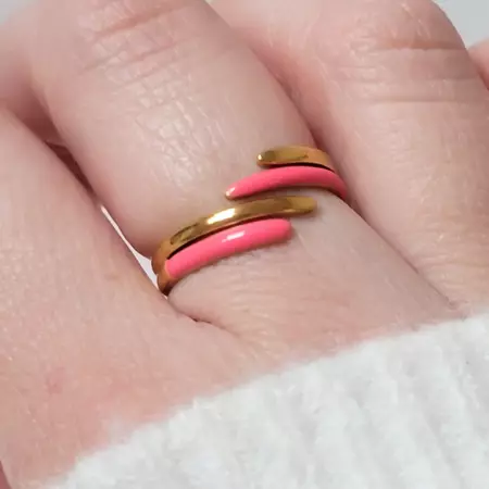 Bague en acier doré et rose fluo portée au doigt sur fond neutre