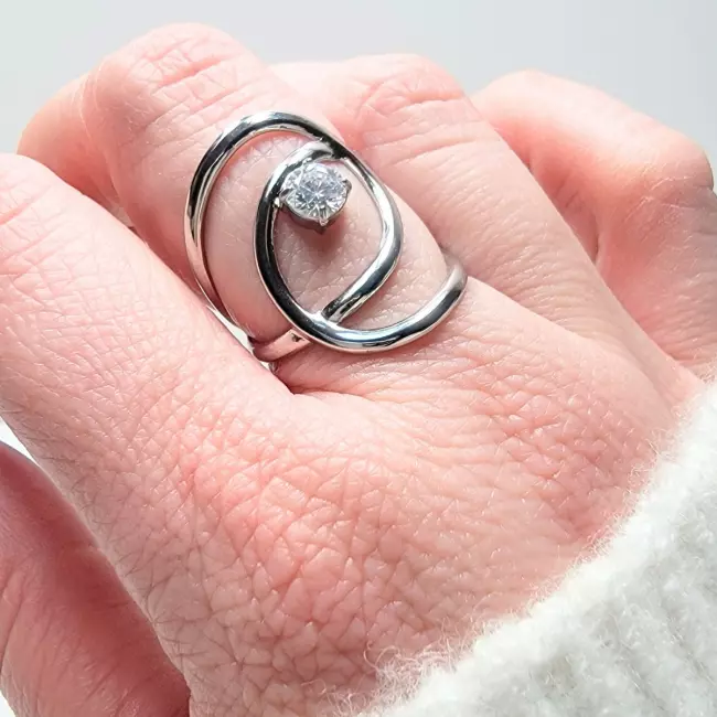 Bague ouverte en acier inoxydable doré et argenté avec pierre brillante, au design entrelacé moderne, présentée sur fond décoratif.