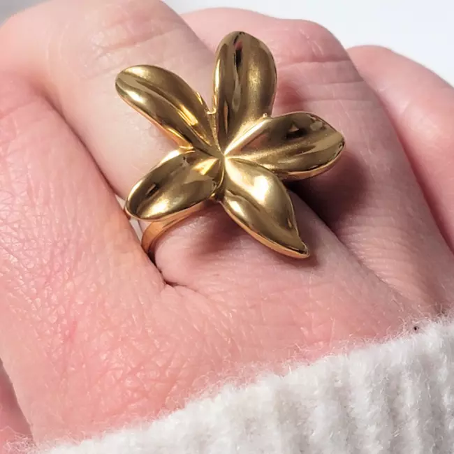 Bague fleur dorée portée sur doigt, finition bombée et élégante