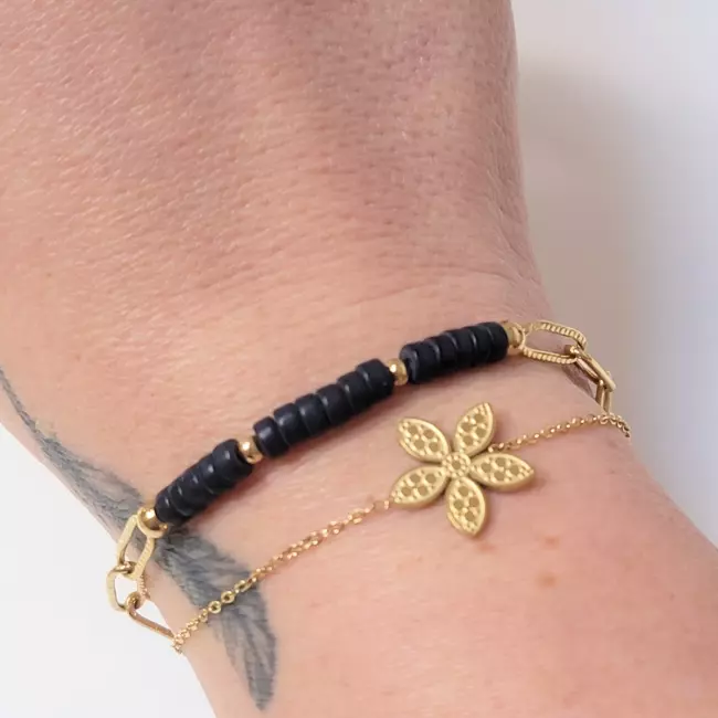 Bracelet noir et doré porté au poignet avec fleur dorée centrale – bijou chic femme
