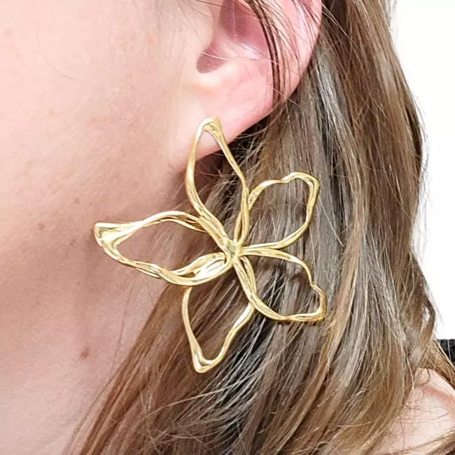 Boucle d’oreille dorée en forme de fleur portée à l’oreille, mise en valeur par la lumière naturelle