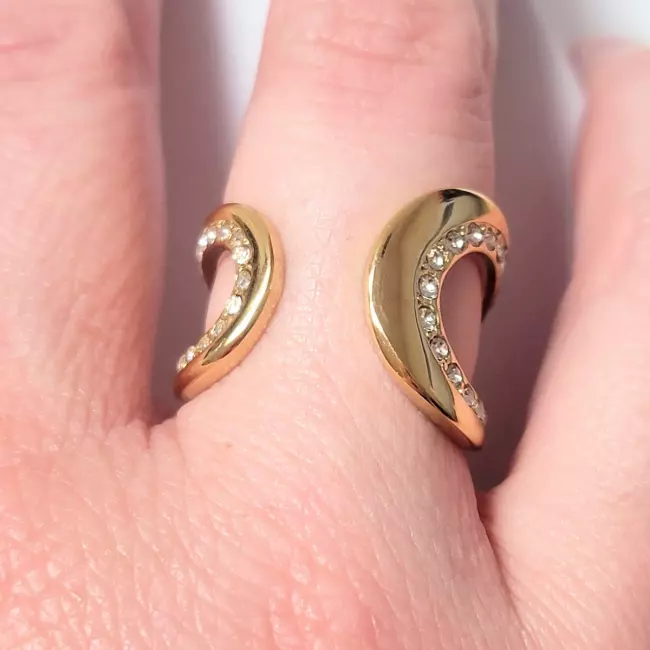 Bague ouverte dorée portée sur main femme, détails brillants visibles