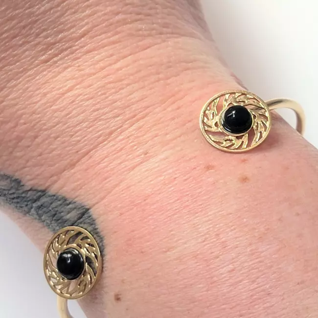 Bracelet jonc doré porté au poignet avec pierres noires et détails ajourés