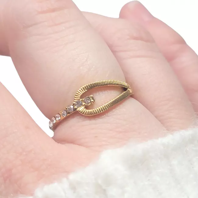 Bague dorée portée au doigt, avec design elliptique et strass, en lumière naturelle