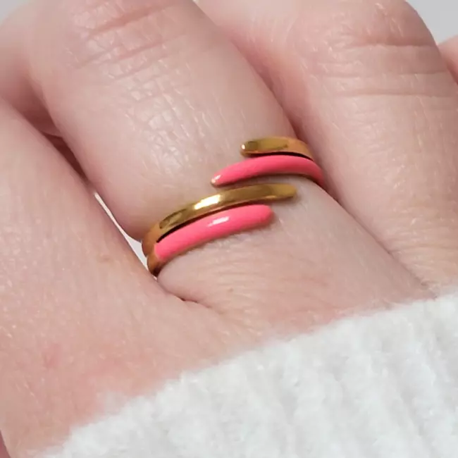 Bague en acier doré et rose fluo portée au doigt sur fond neutre
