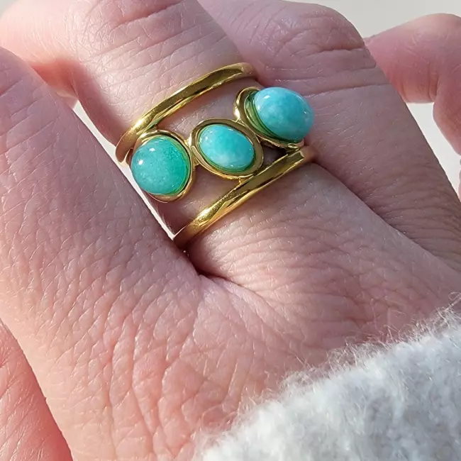 Bague dorée ajustable avec trois pierres naturelles bleu turquoise, posée sur un fond blanc avec un bouquet de fleurs séchées.