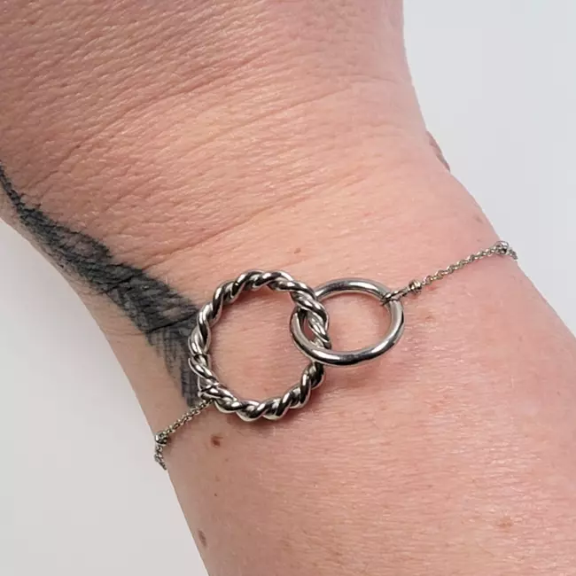 Bracelet minimaliste en acier inoxydable porté au poignet, avec anneaux entrelacés